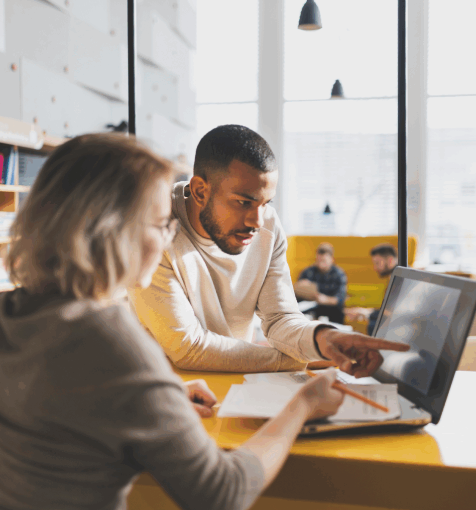 Two colleagues working together behind a laptop with one pointing at the screen