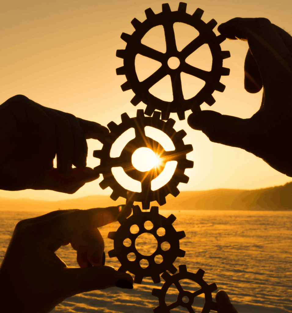 Hands holds cogs up in a line against a sunset depicting smooth operations