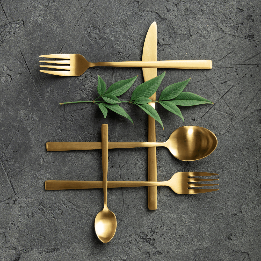Interlacing gold cutlery against black slate with a small branch of green leaves to illustrate vertical integration